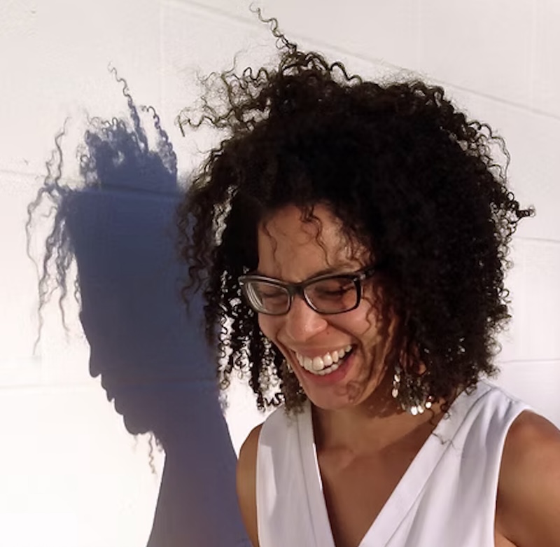 Lisa Jarret smiling in front of a white wall with her shadow to the left.
